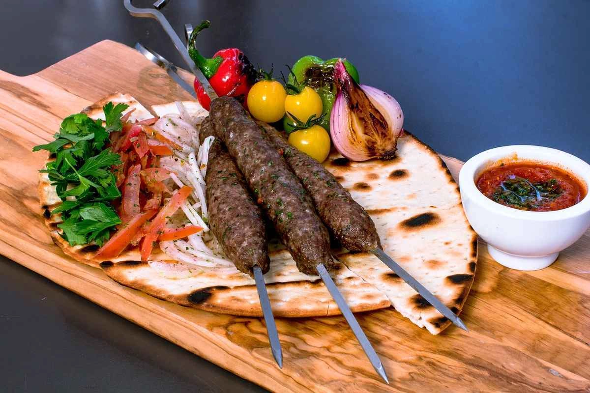 Grilled kebabs served on flatbread with fresh herbs and vegetables